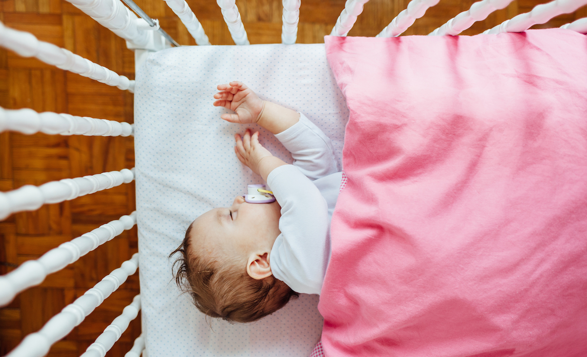 Child sleeping in crib with pink blanket