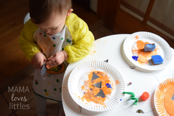 Toddler making pumpkin plate craft and using black construction paper.