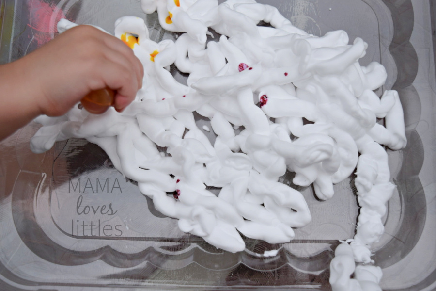 child's hand squirting food coloring onto shaving cream spread out in a pan