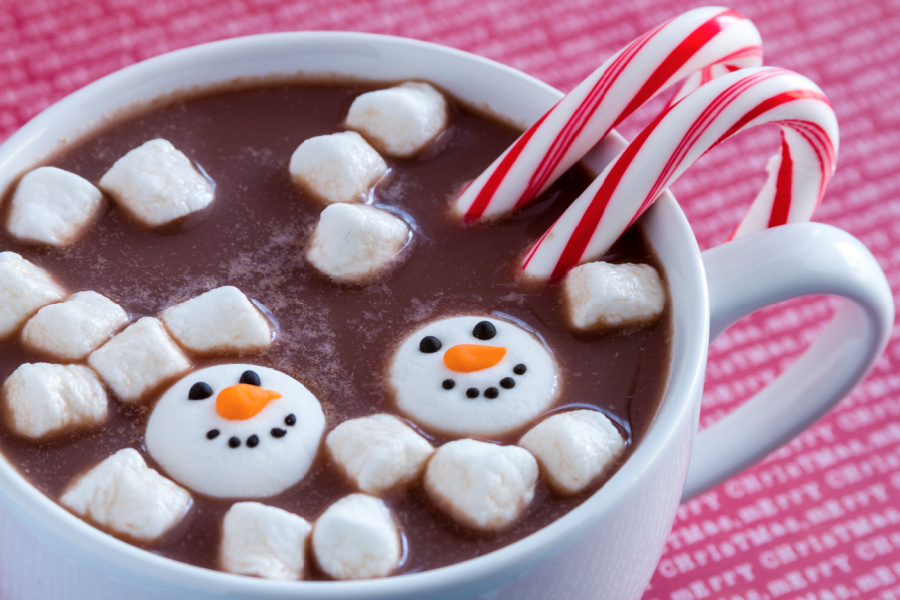 White mug filled with hot chocolate with snowman shaped marshmallows and peppermint candy canes