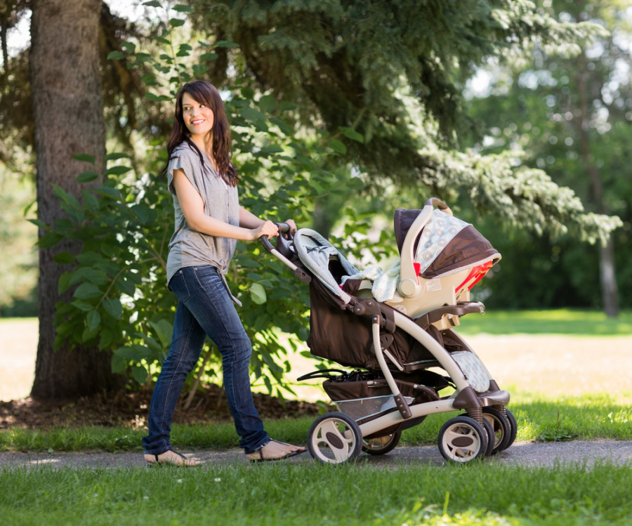 woman pushing baby carriage in park with trees and green grass