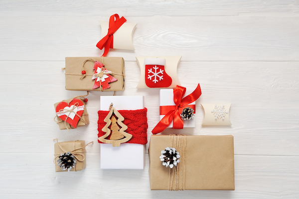 Christmas gift boxes wrapped with white wrapping paper and paper kraft and tied with red ribbons and bakers twine on a white wooden table. 