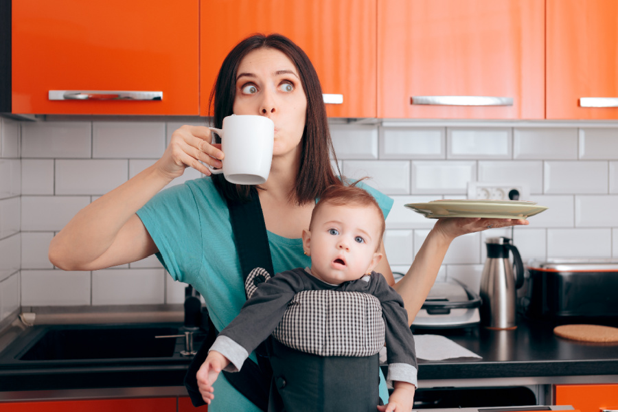 mom drinking coffee while baby wearing in kitchen and looking stressed out