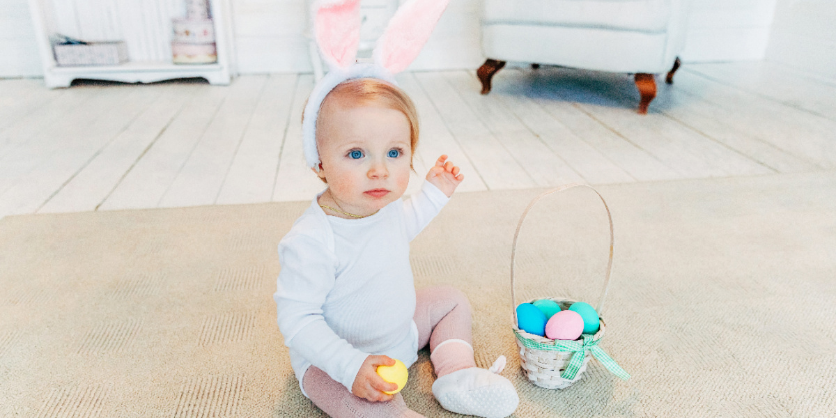 Baby wearing bunny ears next to Easter basket