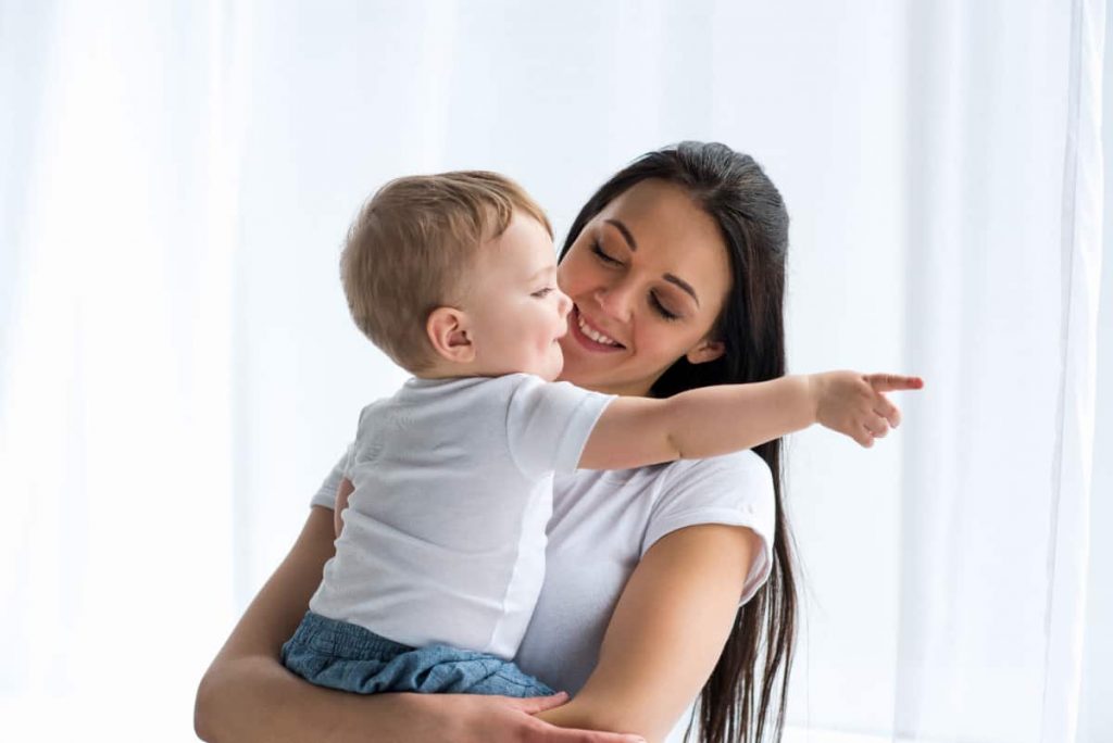 Mom holding toddler who is pointing to communicate