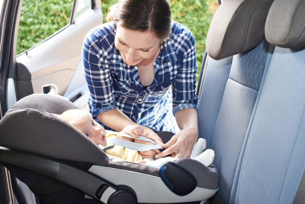 Mom leaning over to buckle newborn baby into carseat