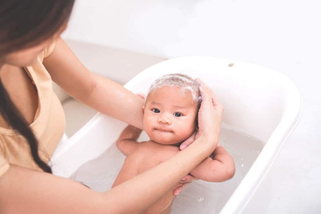 Mom washing newborn baby in tub